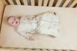 Smiling baby in the cream Eucalyptus sleeping bag on a cot mattress