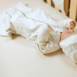 Baby in the Happy Goose 0.5 TOG sleeping bag lying in a cot, side view