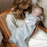 Mother cuddling a baby in the Happy Goose Olive goose print sleeping bag in an armchair