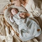 Mother holding the hand of a sleeping baby in the Happy Goose Olive sleeping bag in a basket