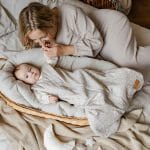 Mama bawi się z niemowlęciem w śpiworku Herbs leżącym w koszu