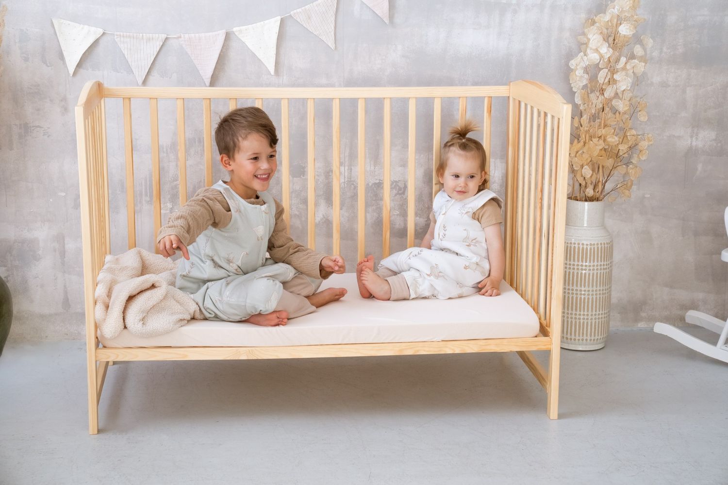 Two children in Happy Goose sleeping bags with legs playing in a wooden cot