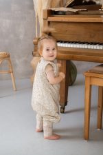 Dziewczynka w śpiworku z nogawkami Herbs stoi przy drewnianym pianinie