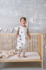 Laughing boy in the Temo sleeping bag with legs standing in a cot
