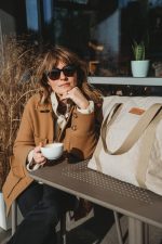 Woman with coffee at a café next to the XL Velvet stroller bag in warm beige