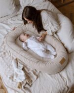 Mother leaning over a baby in the Velvet baby nest in cappuccino