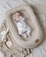 Baby in the Velvet baby nest in cappuccino with a plush bunny beside