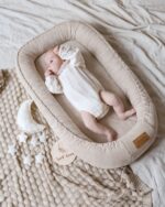 Top view of a baby in a white bodysuit in the Velvet baby nest in cappuccino