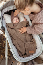 Girl stroking a baby sleeping in a pram under the Bono merino blanket in warm brown