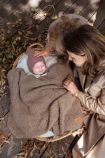 Mother and daughter by a basket with a baby under the Bono merino blanket in warm brown