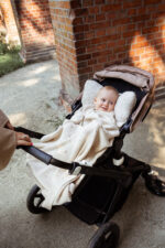 Baby smiling in a stroller covered with the Meri merino blanket in warm beige