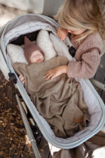Girl hugging a baby in a pram under the Meri merino blanket in warm brown