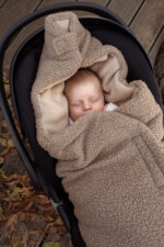 Baby sleeping in a car seat, wrapped in the brown Teddy swaddle with a beige fleece lining