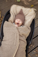 Yawning baby in a knitted hat wrapped in the brown Teddy car seat swaddle