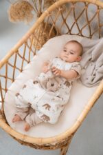 Baby in the Temo sleeping bag with legs lying in a wicker bassinet with a soft toy
